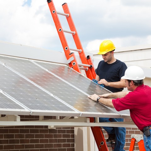 two men in hard hats installing solar panels to a building