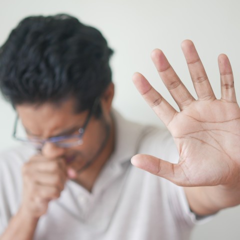 man coughing and holding his hand in front of his face